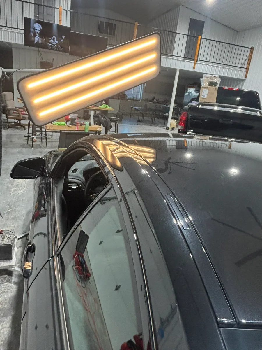 Vehicle roof with LED line-board stripes revealing hail damage on a dark vehicle