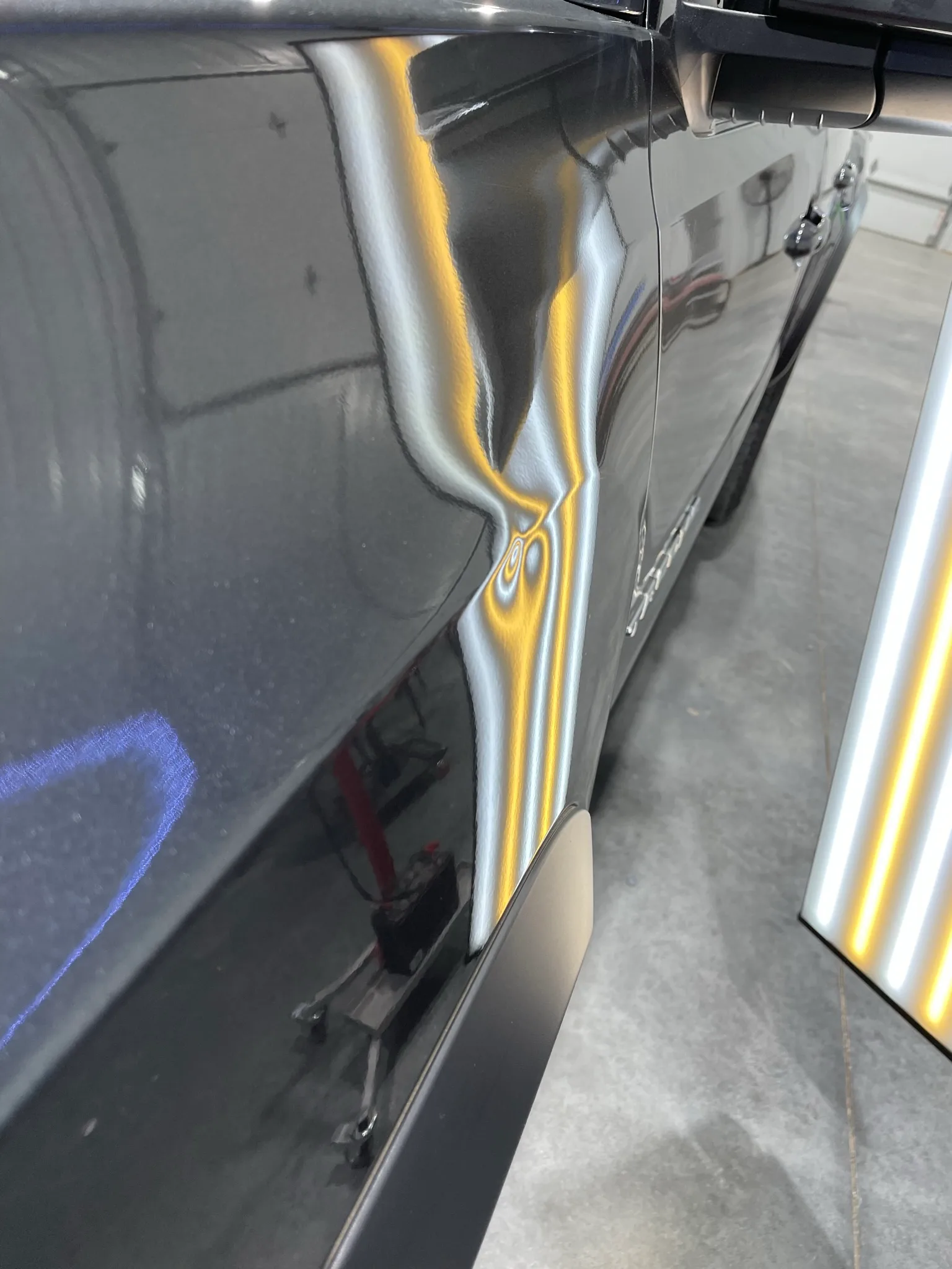 LED line board revealing hail dents on a dark vehicle hood at the Hail Solutions shop in Olathe, Kansas