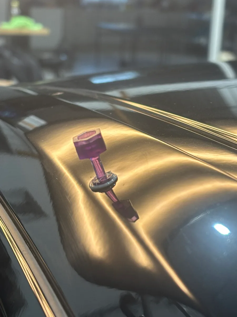 Glue-pull tab bonded to a dark vehicle panel mid-repair of a hail dent