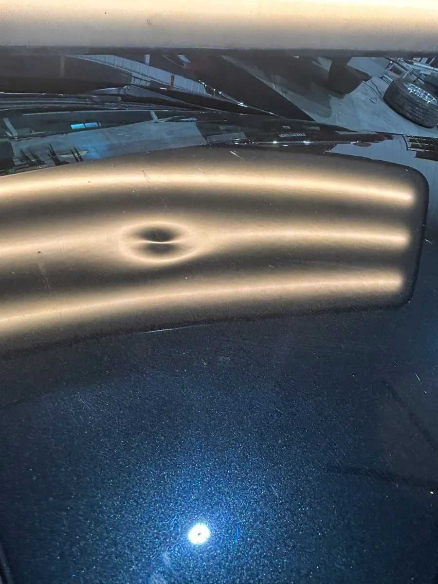 Severe hail dents on a vehicle hood with LED reveal showing the radial pattern
